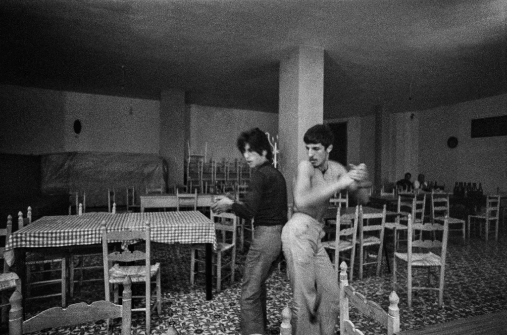 Maschi liberati. Marialba Russo e lo sguardo rovescio sulla mascolinità Due uomini ballano in un ristorante nella fotografia Al ristorante di Marialba Russo, 1974
