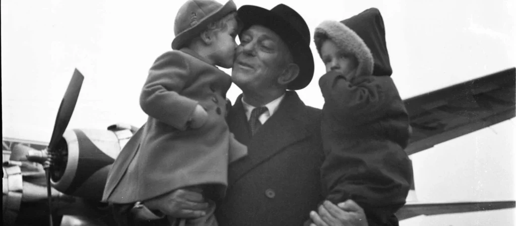 Albert Plesman in cappotto e cappello tiene in braccio due bambini davanti a un aereo a elica della KLM