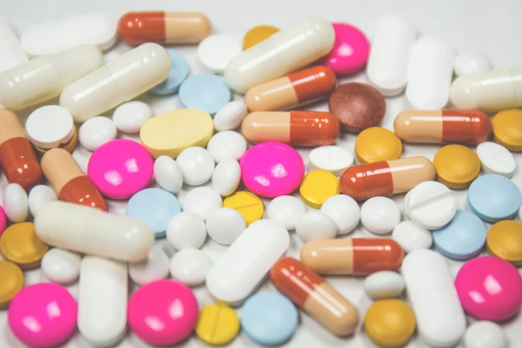 Compresse e capsule di farmaci di diversi colori su una superficie bianca