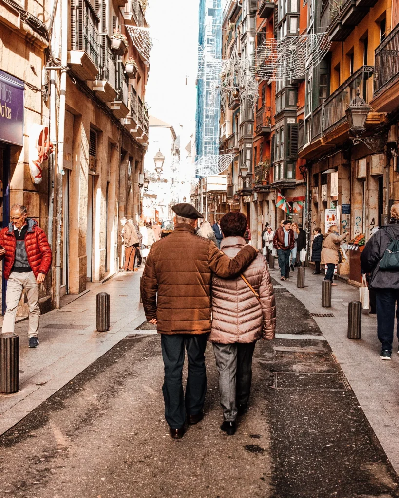 Vivere più a lungo diventerà un lusso? Una coppia di anziani cammina per una strada della città in una giornata di sole