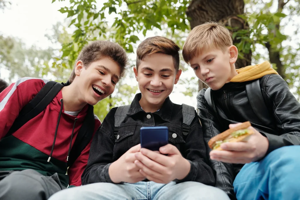 Social vietati ai minori, tre ragazzi adolescenti guardano insieme uno smartphone all'aperto