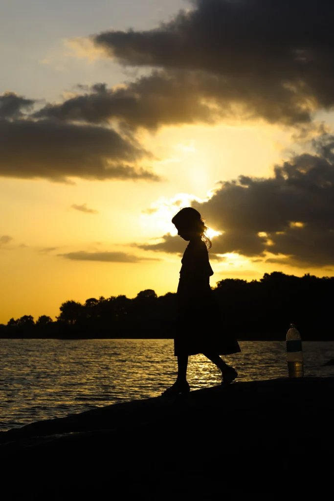 Sagoma di una bambina che cammina in riva a un lago al tramonto