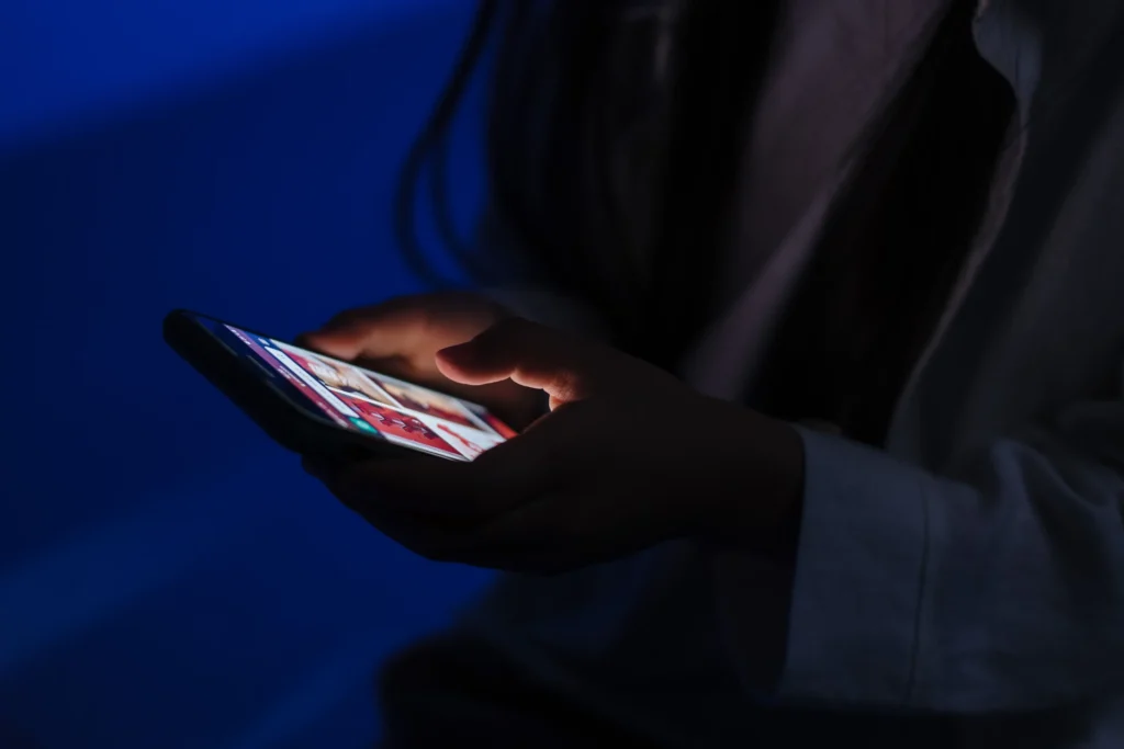  Un ragazzo guarda lo smartphone in una stanza in penombra
