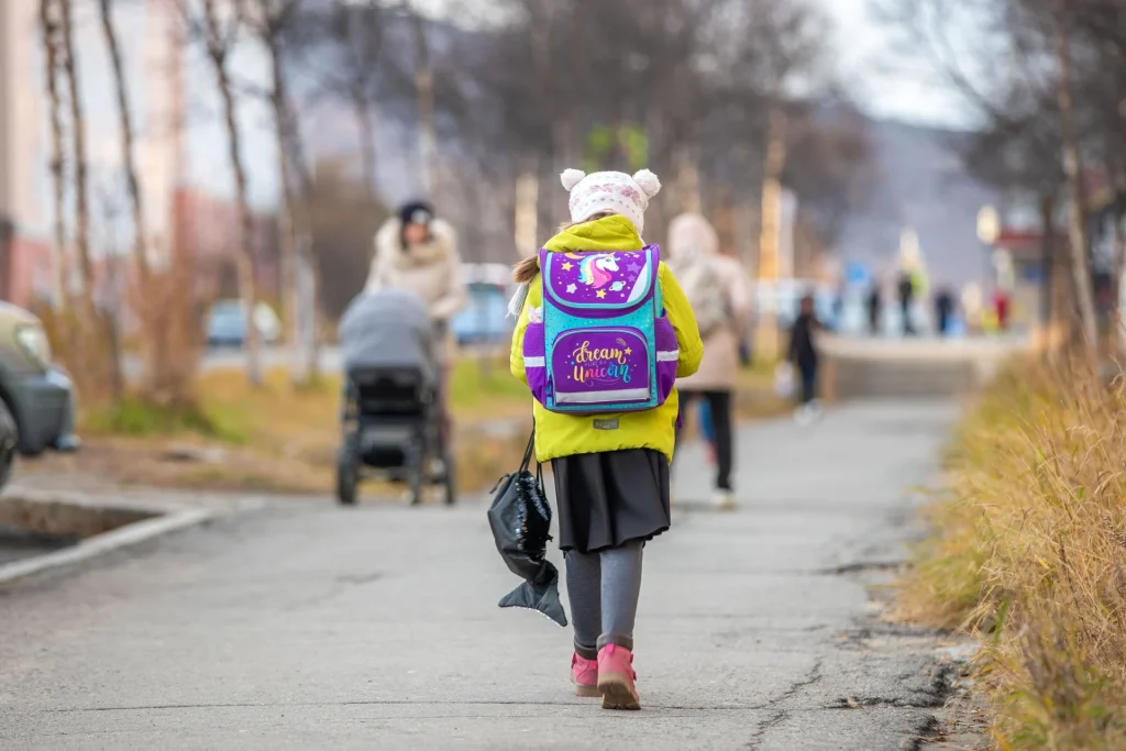 Una bambina cammina verso scuola con uno zaino colorato lungo una strada d’autunno
